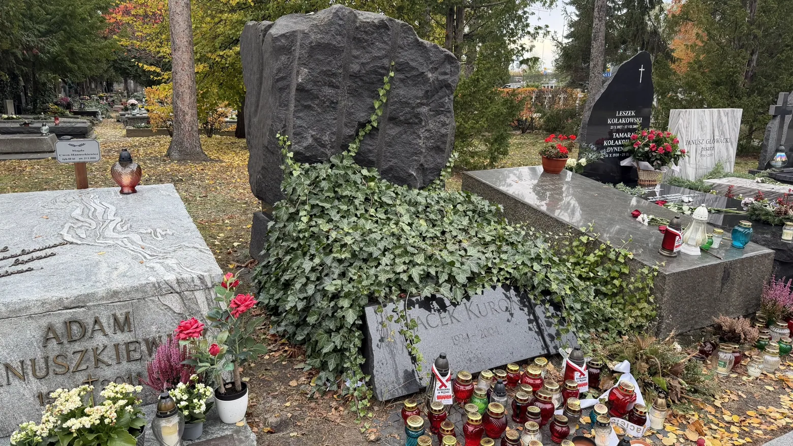 Jacek Kuroń’s ivy-covered grave is central in the photograph; Adam Hanuszkiewicz’s grave is partly visible on the left.